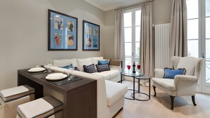 Ein modernes Wohnzimmer mit Sofa, Sessel, Esstisch und einem Kunstwerk an der Wand.