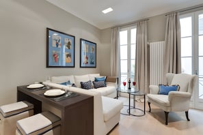 A modern living room with a sofa, armchair, dining table, and artwork on the wall. - Beautiful Apartment in the Heart of Oltrarno (Firenze)