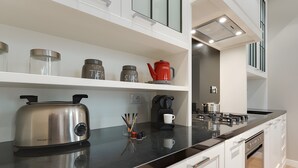 Eine moderne Küche mit schwarzem Arbeitsplatz, Edelstahltoaster, Kaffeemaschine und Glasbehältern auf weißen Regalen.