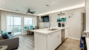 A modern kitchen with a central island, built-in dishwasher, and a flat-screen TV mounted above the island. - NEW | Beachfront | Heated Pools | Hot Tub| Balcony|Ocean Views | Patio | Grills | Cabanas | Pets OK (Galveston)