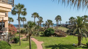 A resort with a pathway leading to a pool area surrounded by palm trees and a view of the ocean. - NEW | Beachfront | Heated Pools | Hot Tub| Balcony|Ocean Views | Patio | Grills | Cabanas | Pets OK (Galveston)