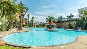 A swimming pool with lounge chairs and palm trees. - NEW | Beachfront | Heated Pools | Hot Tub| Balcony|Ocean Views | Patio | Grills | Cabanas | Pets OK (Galveston)