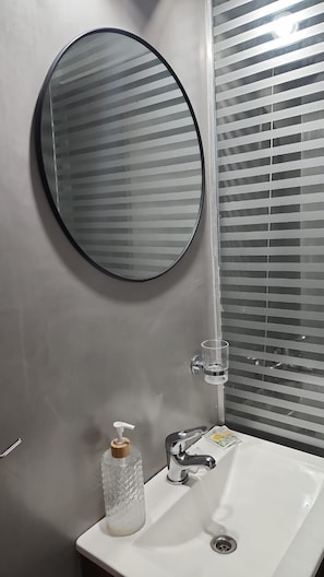 Ein Badezimmer mit einem runden Spiegel, einem weißen Waschbecken, einem Seifenspender und einem Glas Wasser.