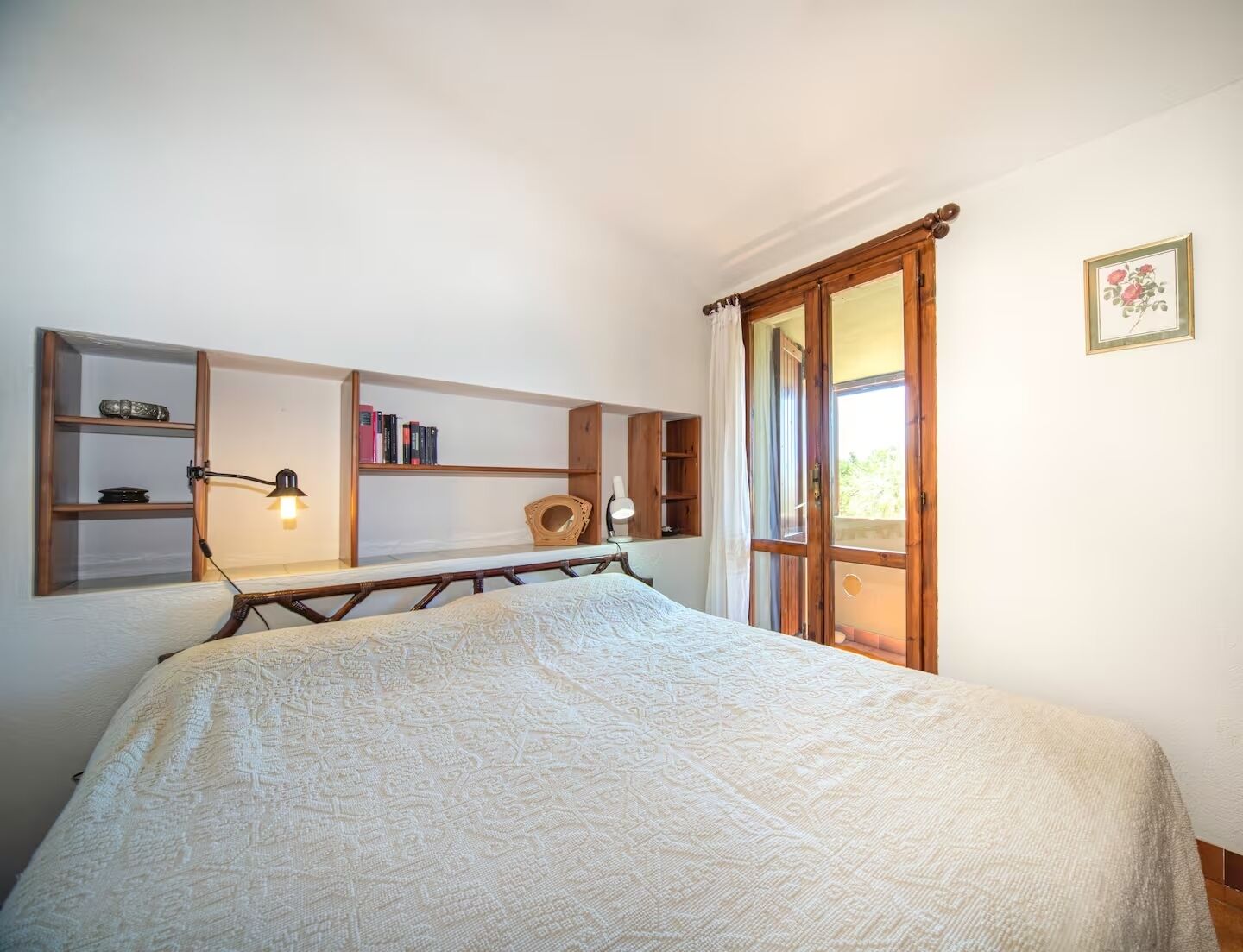 A bedroom with a bed, wooden shelves, a desk, and a window with curtains.