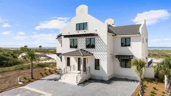 A two-story white building with a balcony, a covered entryway, and a view of the beach. - Rumor Has It: Beachfront, Private Pool, Pet Friendly, Golf Cart Community (Mexico Beach)
