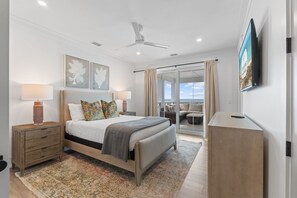 A bedroom with a bed, bedside tables, a ceiling fan, a TV, and a view through a glass door. - Shuck Yeah!: Beachfront home with Private Pool located in Sugar Sands community! (Mexico Beach)