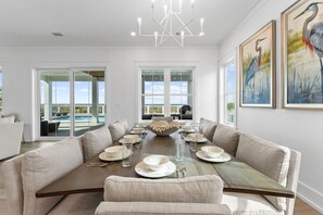 A dining room with a long table set for six, large windows, and a view of the outdoors. - Shuck Yeah!: Beachfront home with Private Pool located in Sugar Sands community! (Mexico Beach)