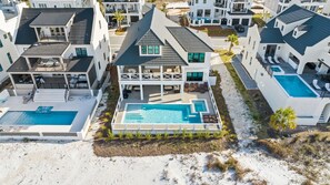 A modern multi-story house with a large swimming pool, multiple balconies, and a beachside location. - Shuck Yeah!: Beachfront home with Private Pool located in Sugar Sands community! (Mexico Beach)