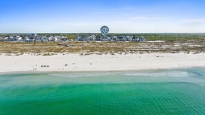 Ett flygbildsbild av ett kustområde med en rad fastigheter som ligger vid stranden, en sandstrand och klart, turkosfärgat vatten.