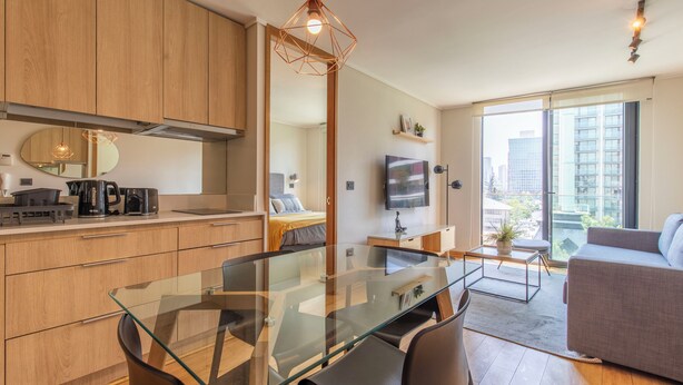 Un appartement moderne doté d’une table à manger en verre, de meubles en bois, d’un canapé et d’une grande fenêtre offrant une vue sur la ville.