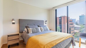 Une chambre moderne avec un grand lit, une table de chevet, une chaise et une vue sur la ville par la fenêtre.