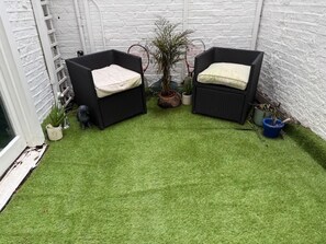 Un petit espace patio avec deux chaises en osier noir, une petite plante en pot et un mur en briques blanches.