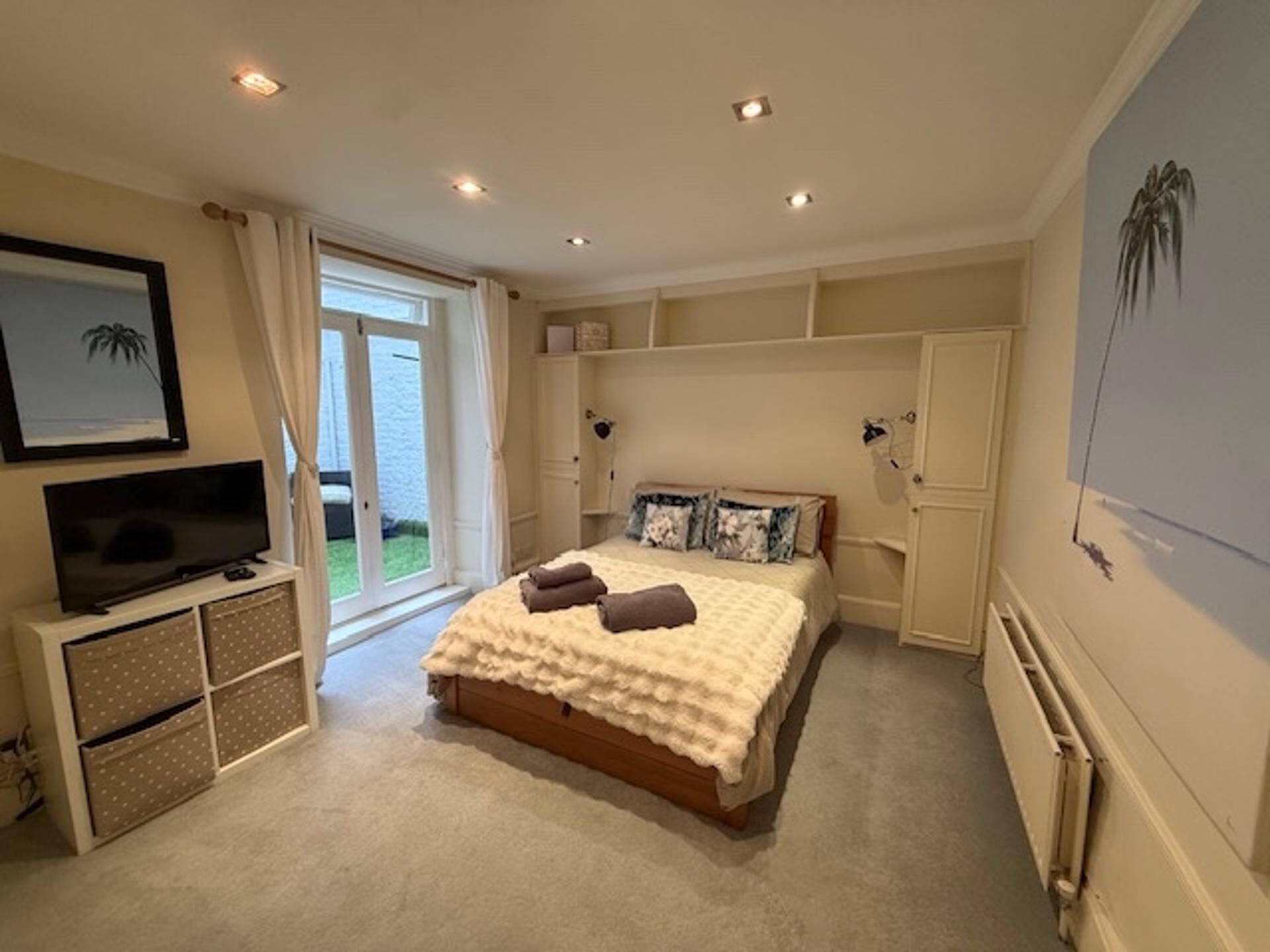 Une chambre à coucher comprenant un lit, un téléviseur, un meuble de rangement et donnant sur l’extérieur.