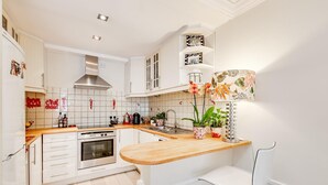 Eine moderne Küche mit weißen Schränken, einem eingebauten Ofen, einer Holz Arbeitsplatte und einem weißen Stuhl.