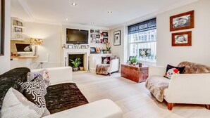 Ein modernes Wohnzimmer mit Kamin, weißen Sofas, einem Flachbildfernseher und einem großen Fenster.