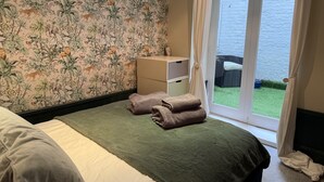 Ein Schlafzimmer mit grüner Bettdecke, einem weißen Kopfkissen und Tapete mit Leopardenmuster. Ein Fenster mit Vorhängen bietet Blick aufs Meer.