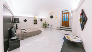 Un espai habitable compacte amb un sofà, una taula de dinar amb cadires, una petita cuina i una porta que dona a una zona exterior.