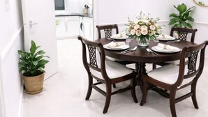 A dining area with a round table set for four, surrounded by wooden chairs with cushioned seats. There is a vase with flowers on the table, and a potted plant is visible to the side. - Stylist 7sleeps contractor groups friendly1bedroom flat Canada Water free WiFi (London)