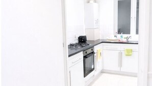 A bright kitchen with white cabinets, a black countertop, and a window. - Stylist 7sleeps contractor groups friendly1bedroom flat Canada Water free WiFi (London)