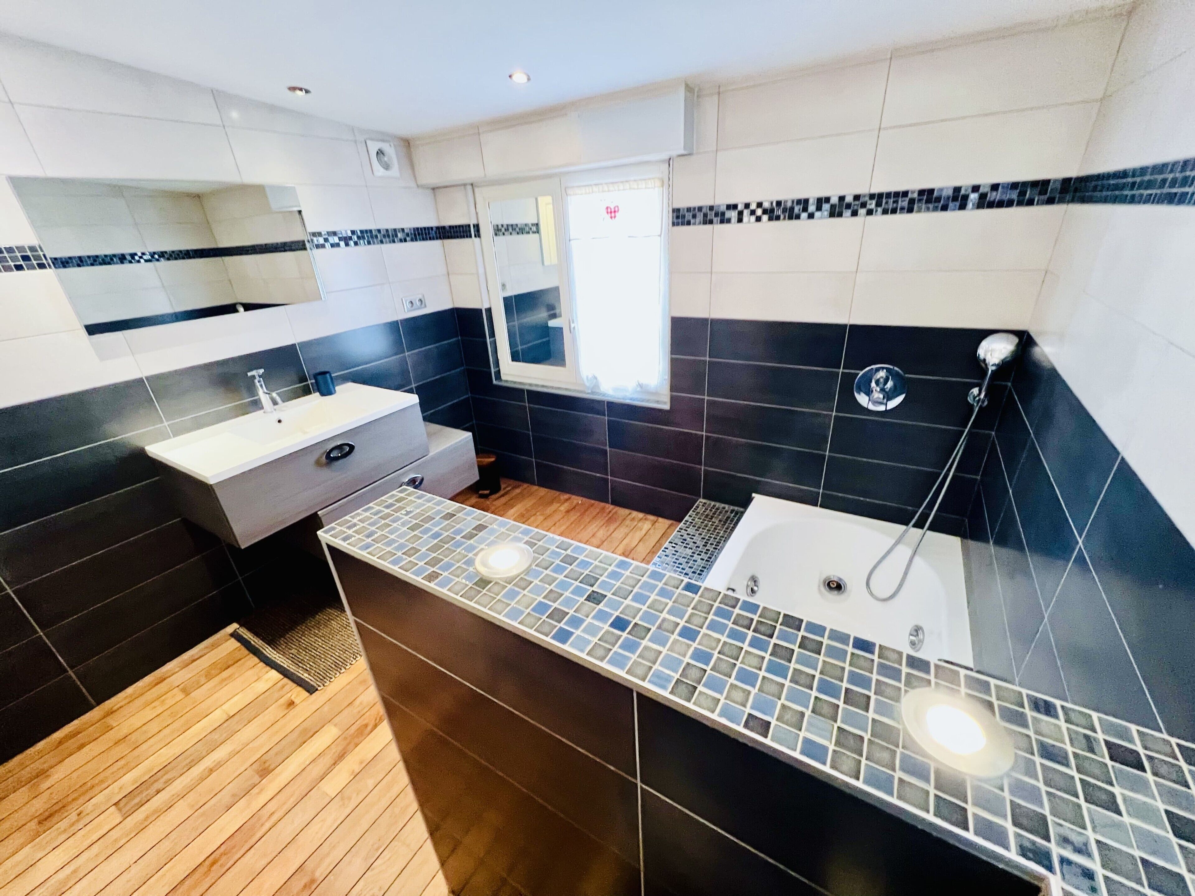 Une salle de bain moderne avec un plancher en bois, un lavabo blanc, un miroir et un espace douche.