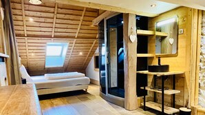 Een gezellig slaapkamer op zolder met dakraam, een bed, een kleine badkamer met spiegel en wastafel, en een houten vloer.