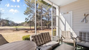 A covered outdoor seating area with a sofa, chairs, and a table, overlooking a natural landscape. - Cypress Bend @ Barefoot - Updated w/ Pools, Golf, Shuttle (North Myrtle Beach)