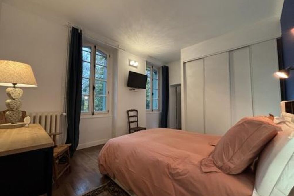 Ein Schlafzimmer mit einem Bett, einem Nachttisch, einer Lampe, einem Sessel, einem Fernseher und einem Fenster.