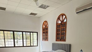 A spacious room with a large bed, two windows with wooden frames, a ceiling fan, and a small table with chairs.