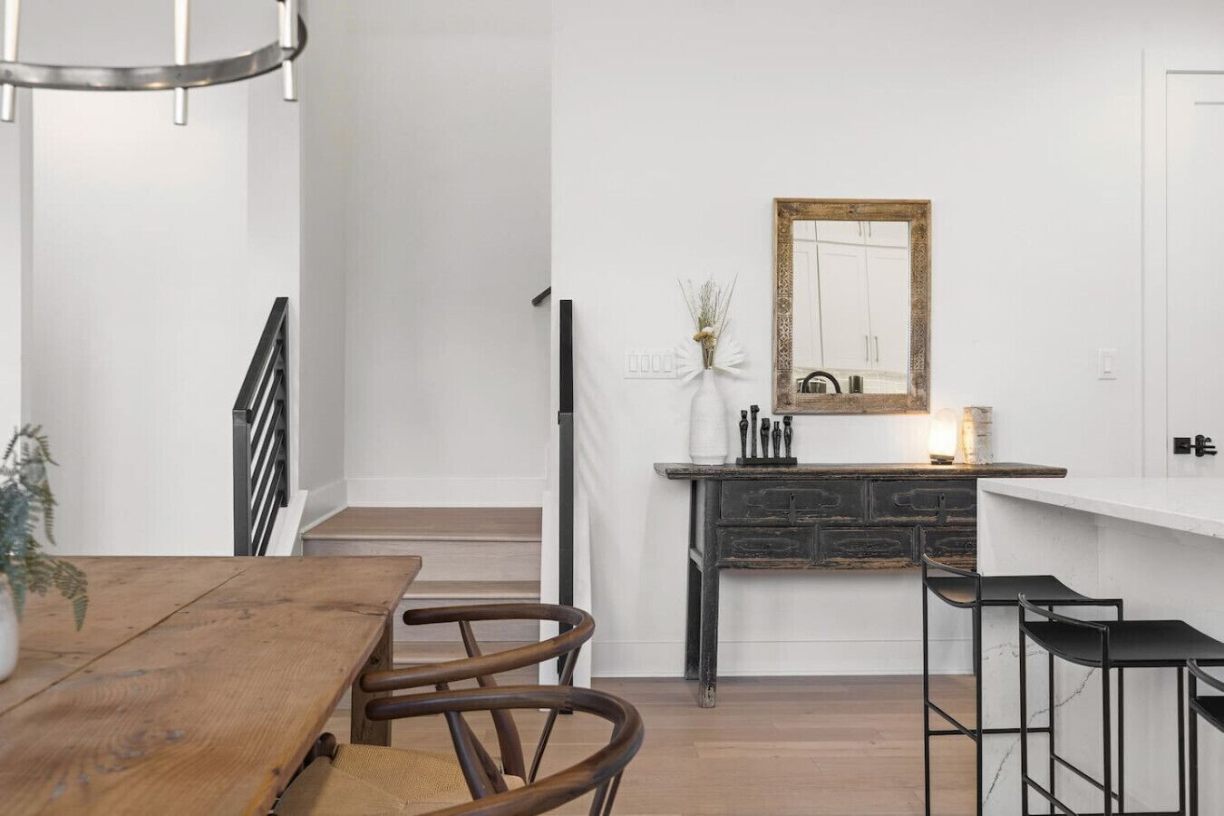 A modern kitchen with a white countertop, a stone backsplash, and a wooden dining table with chairs.
