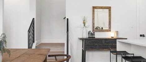 A modern kitchen with a white countertop, a stone backsplash, and a wooden dining table with chairs.