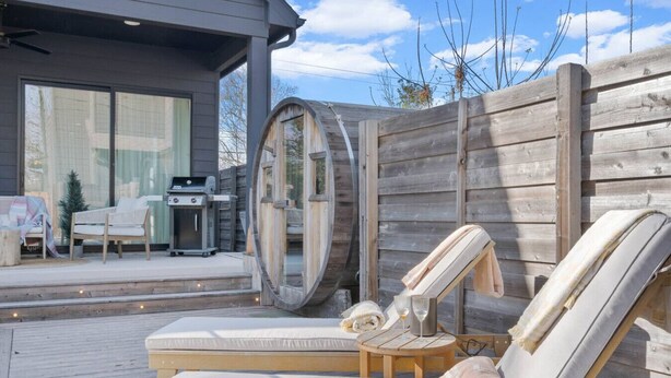 Eine Holzterrasse mit Liegestuhl, einem kleinen Tisch und einem Grill.