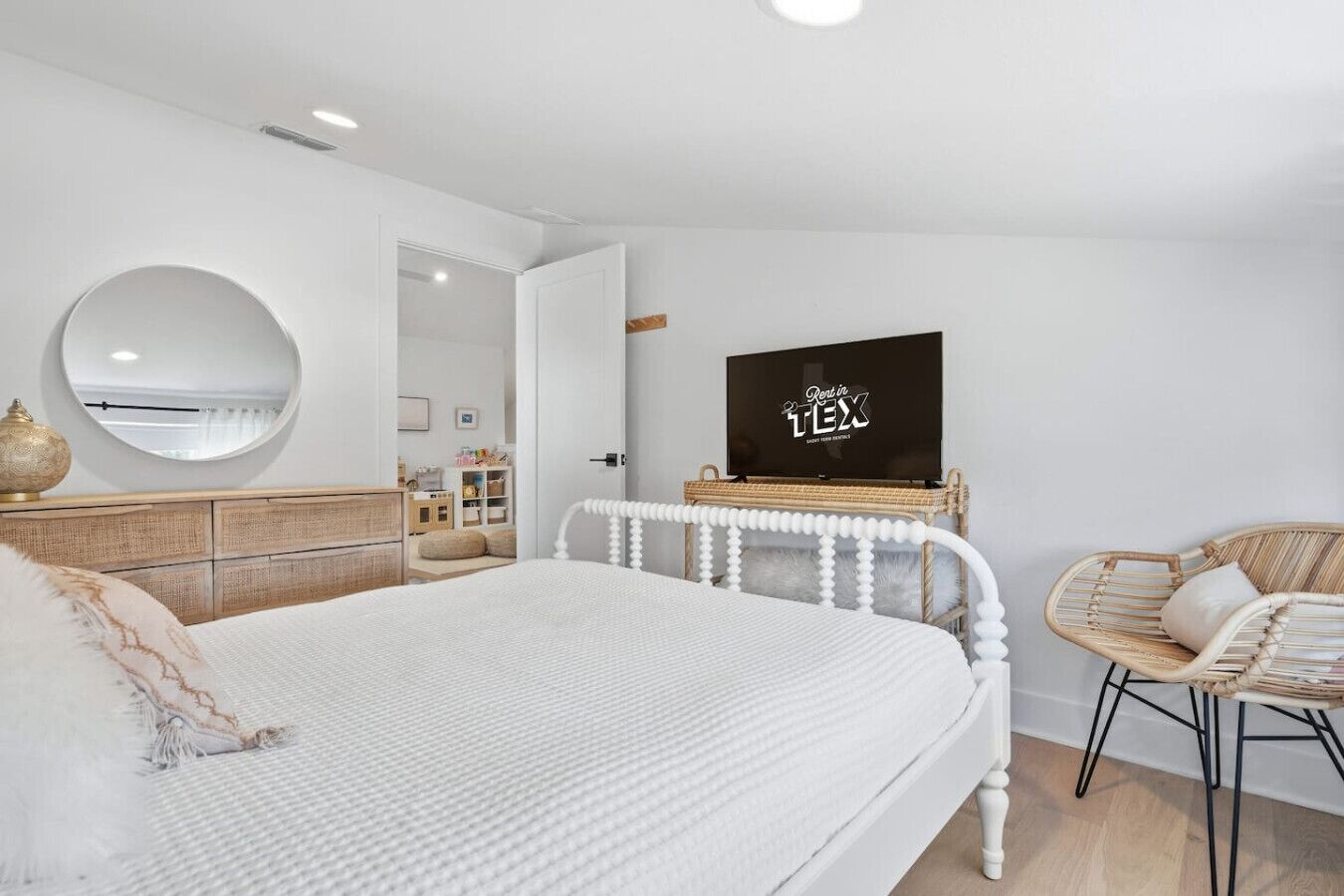 Une chambre à coucher avec un lit, un téléviseur posé sur un meuble en bois, une chaise en osier et un miroir accroché au mur.