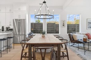 Eine moderne Küche mit weißen Schränken, einem Edelstahlkühlschrank, einem Holzessttisch mit Stühlen und einer Pendelleuchte.