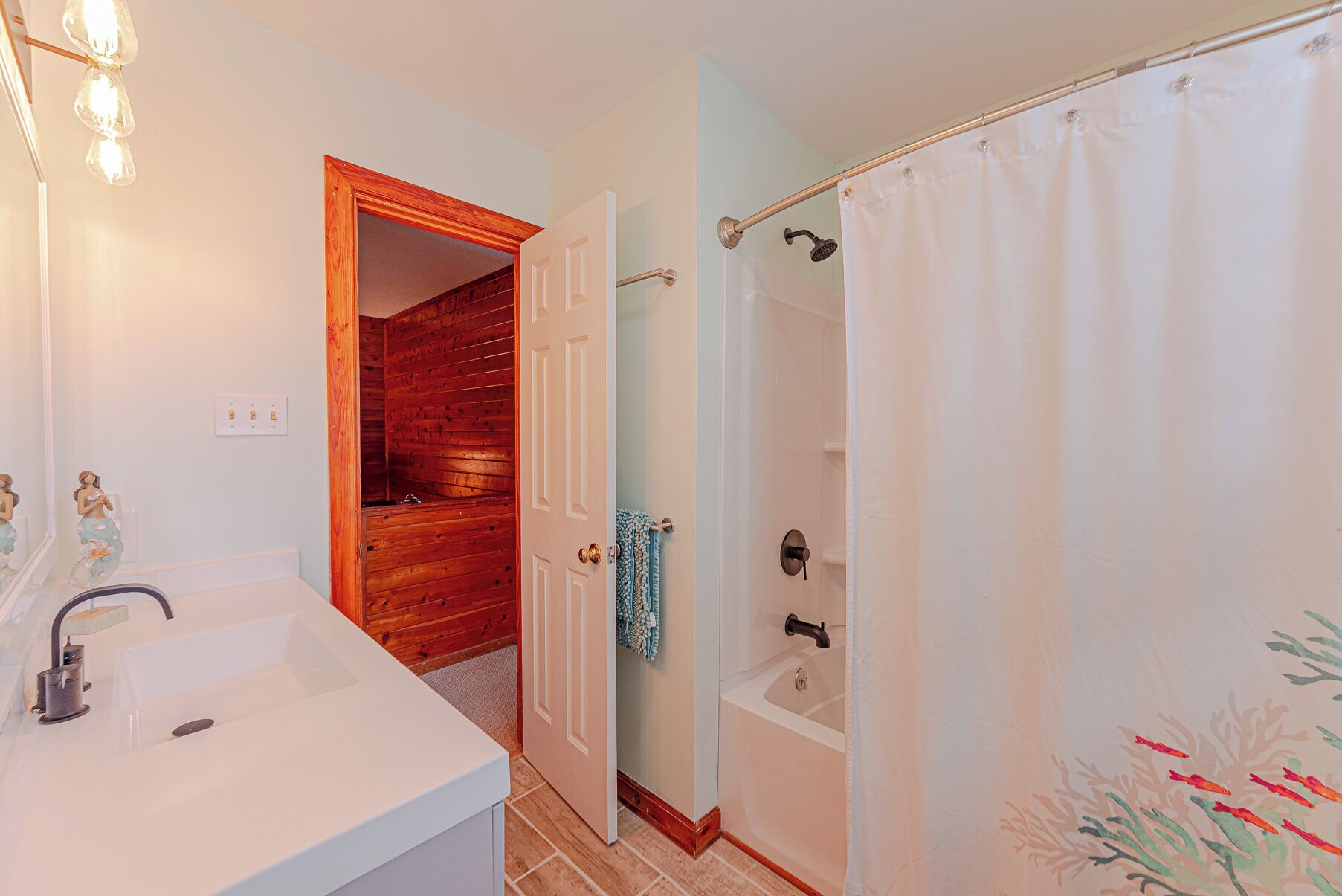 Un bagno con un lavandino bianco, una doccia con tenda e una porta in legno che dà su un'altra stanza.