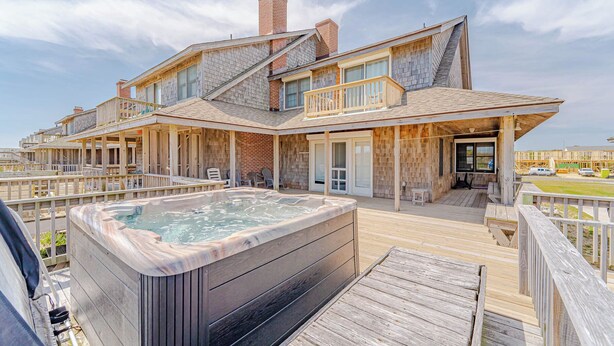 Een tweelaags huis met een jacuzzi op het terras, houten leuningen en uitzicht op de oceaan.