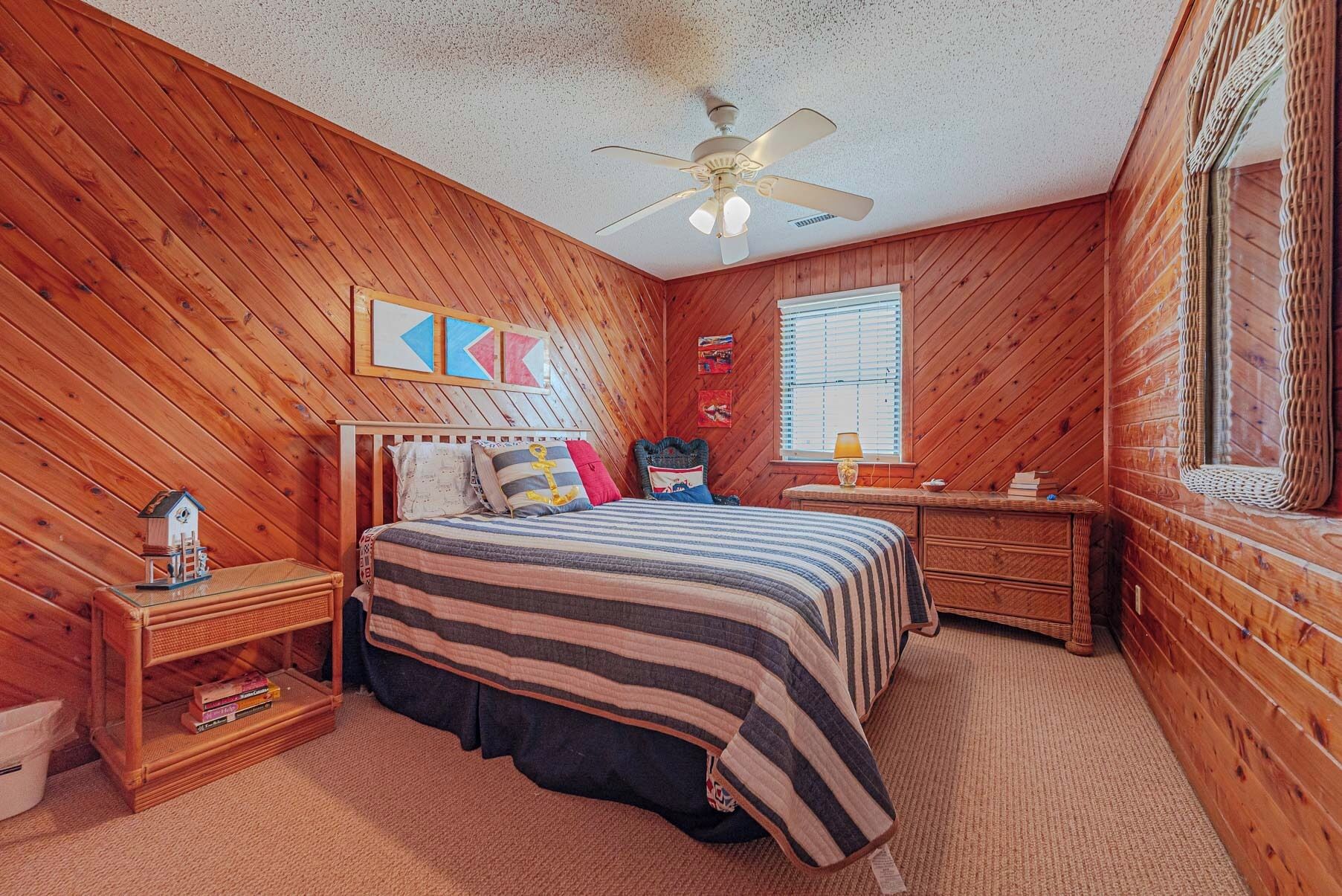 A wooden-paneled bedroom with a bed, nightstands, a ceiling fan, and a window.