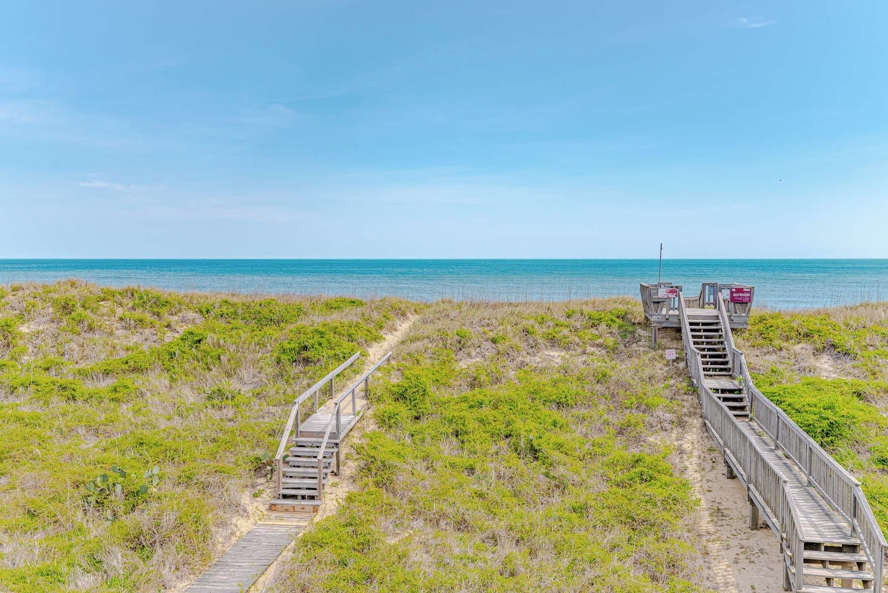 Une promenade en bois qui mène à une plage d’où l’on a une vue dégagée sur l’océan.