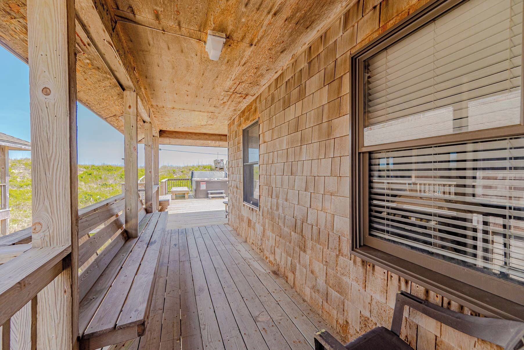 A wooden deck with a covered porch, a grill, and a window with blinds.