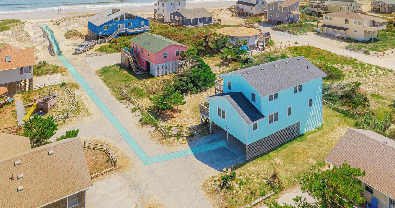 An aerial view of a coastal residential area with houses, a beach, and a pedestrian path.