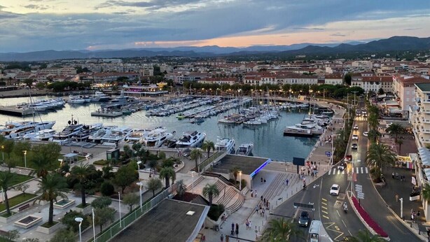Un port de plaisance où sont amarrés de nombreux bateaux, entouré d’un paysage urbain avec des bâtiments et un ciel dégagé.