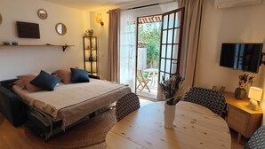 Une chambre à coucher comprenant un lit, une table de chevet, une chaise, un téléviseur et donnant sur l’extérieur.