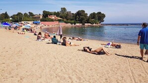 Une plage où l’on peut voir des gens se prélasser au soleil et se baigner, des parasols et des bâtiments situés en bord de mer.