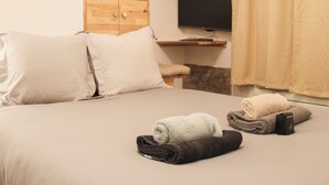 Una cama bien hecha con almohadas, un televisor montado en la pared y un estante de madera encima.