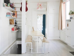 A bright, white interior with a wooden bench and a table, shelves with books and toys, and a window with curtains. - 90m² Flat with Private Garden near Paris (Ivry-sur-Seine)