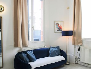 A modern room with a blue sofa, beige curtains, a framed artwork, and a floor lamp. - 90m² Flat with Private Garden near Paris (Ivry-sur-Seine)