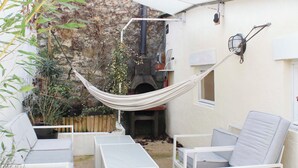 Un patio con mobiliario blanco, una hamaca y un muro de piedra.