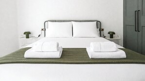 Cama bien hecha con sábanas blancas y dos toallas dobladas sobre un tapete verde.