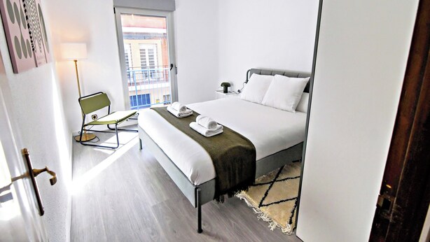 Una habitación de hotel moderna con una cama, un escritorio y una silla. Se ve una ventana con vistas a edificios.