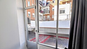 Una habitación con un ventanal grande que da a un patio con piso rojo y balcones con ropa colgada.