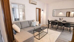 Una sala de estar moderna con un sofá gris, una mesa de centro negra y un comedor con mesa y sillas.